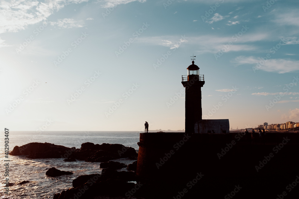 Lighthouse with silhouettes of people in front of sea