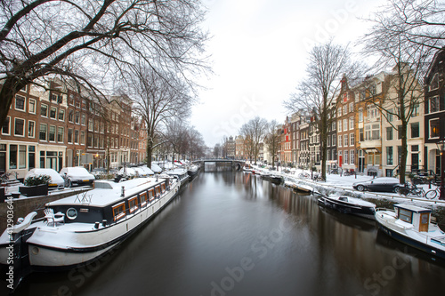 Winter snow view of Dutch canal and old houses in the historic city of Amsterdam, the Netherlands