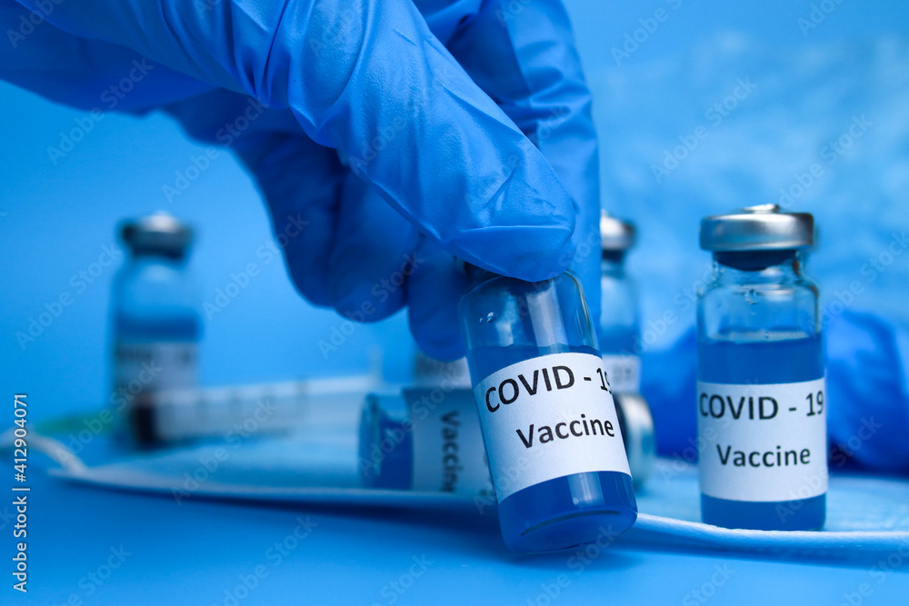 The doctor holds a coronavirus vaccine in hand on a blue background. The concept of the fight against ncov COVID-19 pandemic The doctor holds a coronavirus vaccine in hand on a blue background. The concept of the fight against ncov COVID-19 pandemic