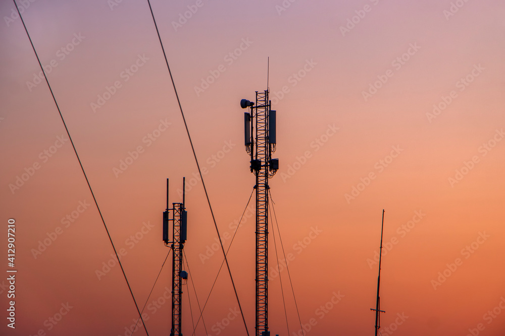 Tower with a mobile signal transmitter on the background of an orange cloudless sky in the morning.