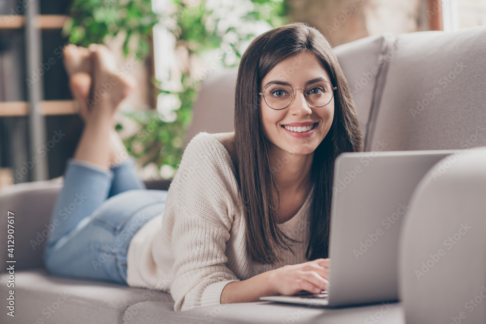 Photo of cheerful positive girl use laptop lie sofa in living room stay home good mood inside house indoors home Photo of cheerful positive girl use laptop lie sofa in living room stay home good mood inside house indoors home