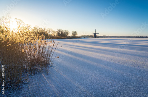 Tranquil winter sunrise over a frozen lake, with a windmill in the distance.