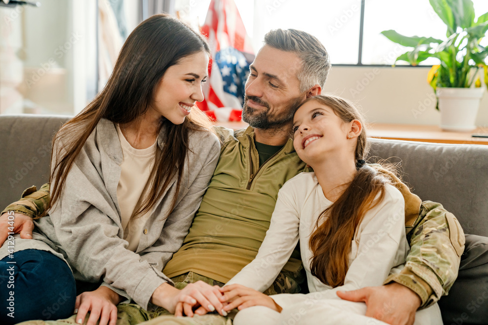 Happy masculine military man hugging his family while sitting on sofa Happy masculine military man hugging his family while sitting on sofa