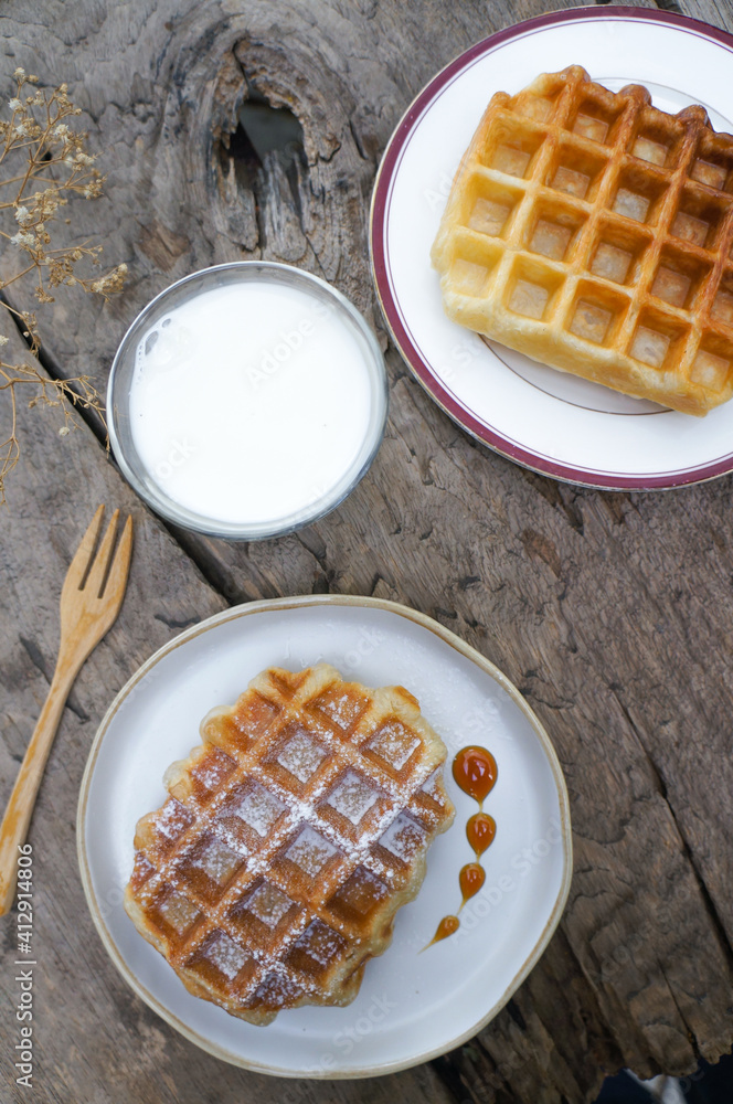 Top view Waffles with caramel syrup in a white plate and fresh milk in a glass placed on the table. Top view Waffles with caramel syrup in a white plate and fresh milk in a glass placed on the table.