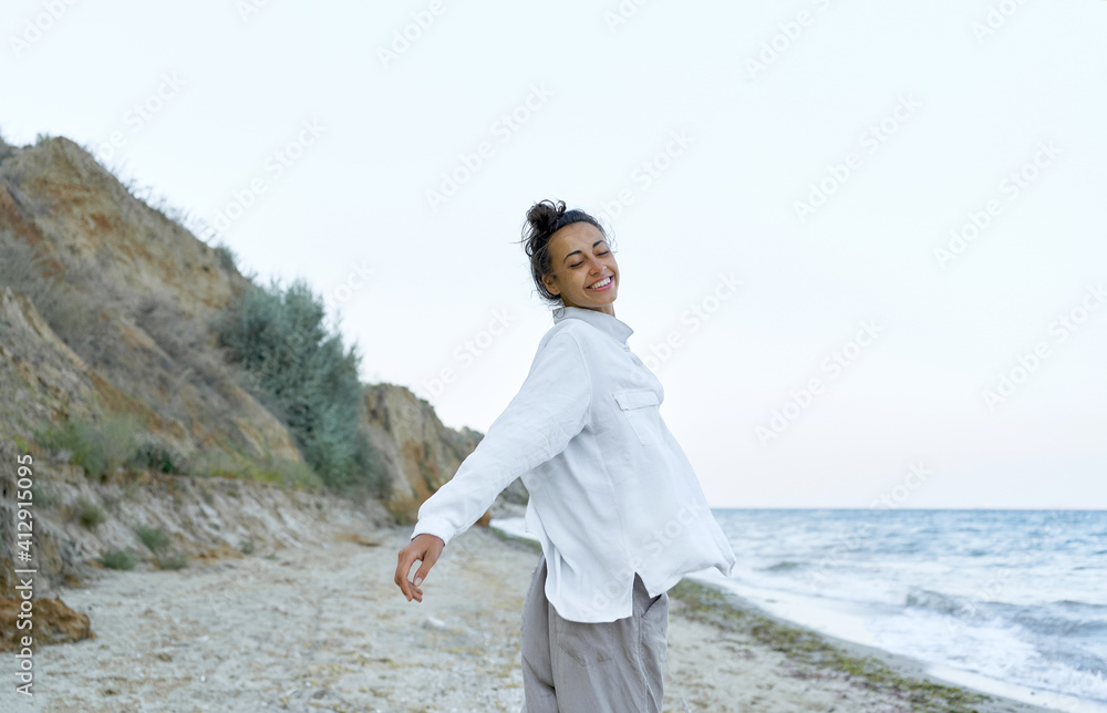 Playful carefree girl in white blowing shirt dancing at wild beach with eyes closed. Concept freedom and authentic emotion Playful carefree girl in white blowing shirt dancing at wild beach with eyes closed. Concept freedom and authentic emotion