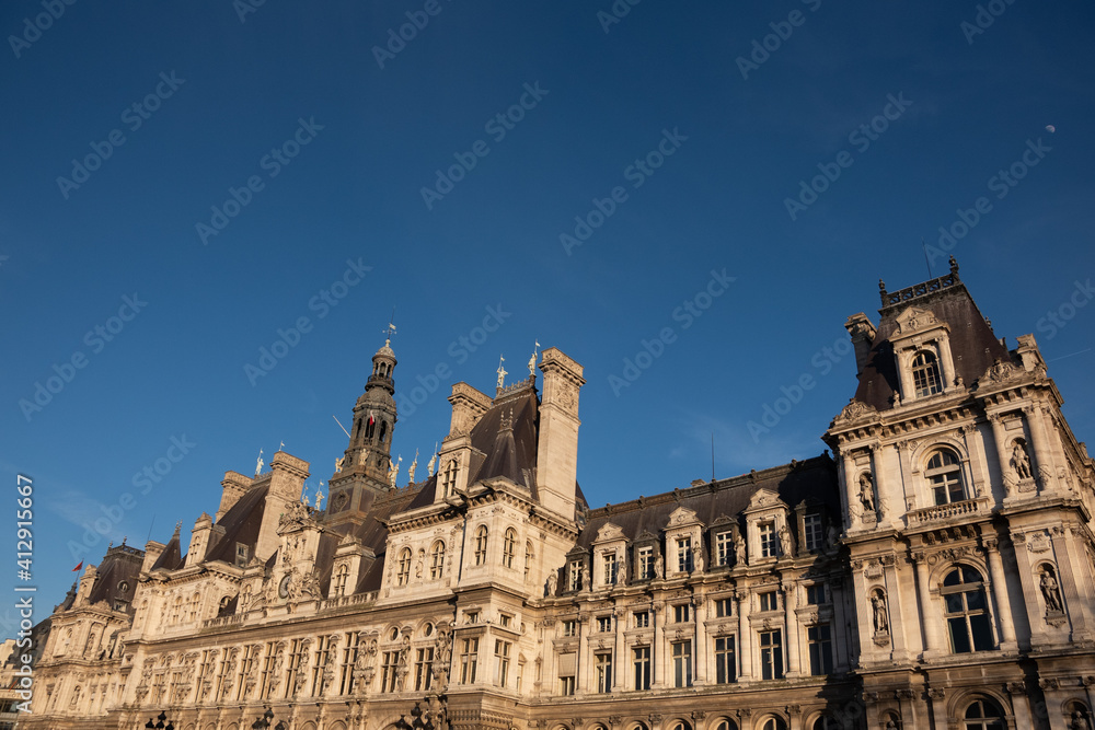 Paris, France. Beautiful Parisian city hall (hotel de ville) in sunset golden lights and moon in dark blue sky and passing plane trace. Travel background. Europe capitals tourism concept.