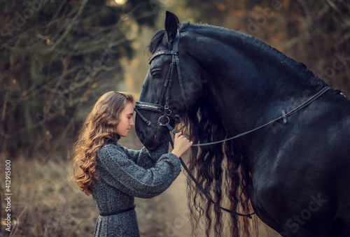 Beautiful girl staying near black Frisian horse in spring in the forest