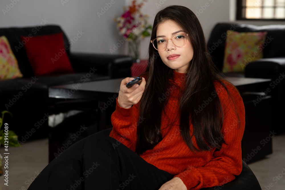 Pretty young woman holding TV remote control in her hands sitting in her living room, Attractive girl adjusting Television controls. Pretty young woman holding TV remote control in her hands sitting in her living room, Attractive girl adjusting Television controls.