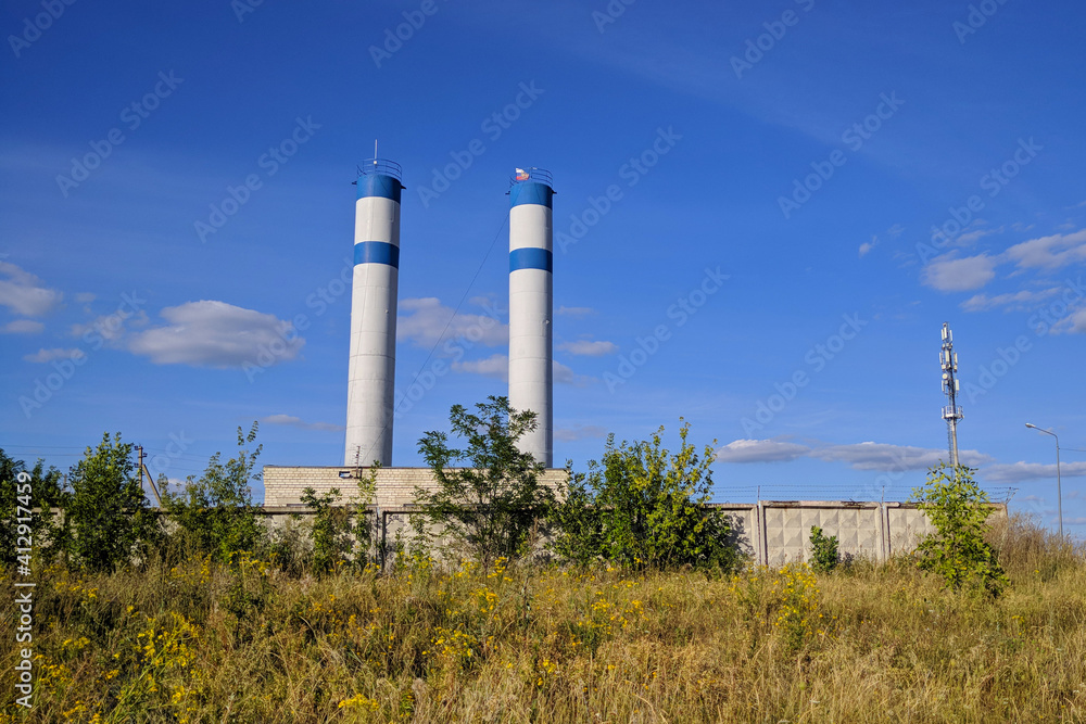 Two round metal towers with antennas in an overgrown dry area of grass and trees