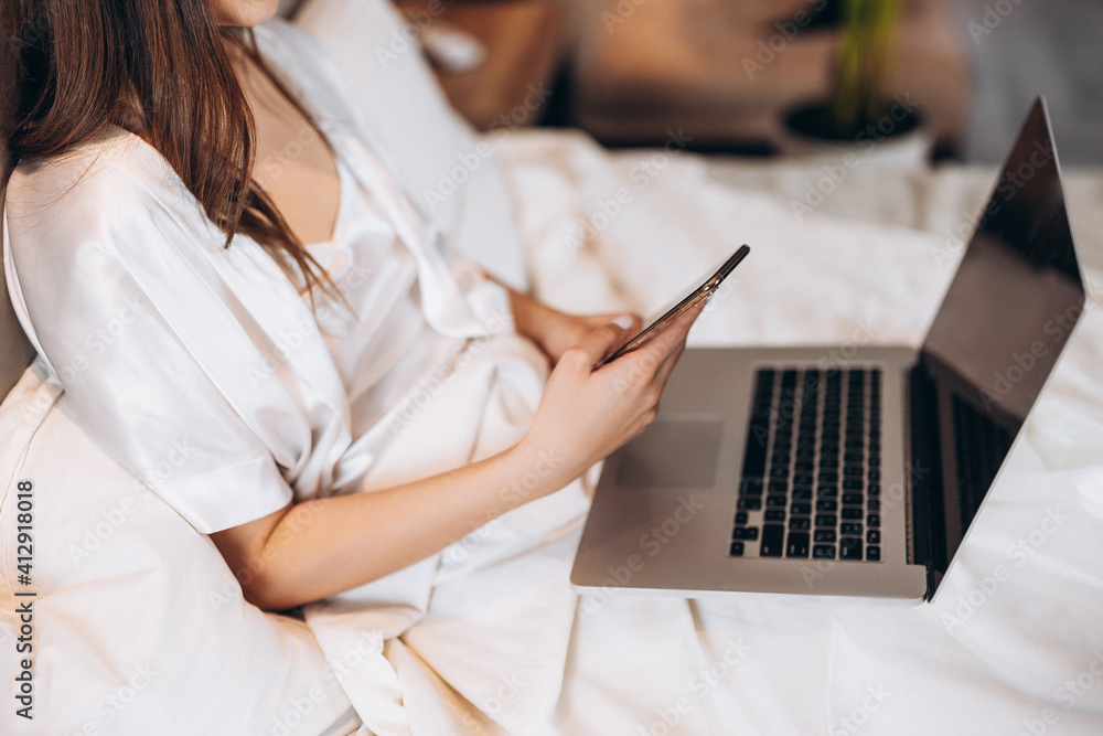 Fototapeta premium laptop and phone in the hands of a woman without a face. laptop and phone on the background of white pajamas. work at home