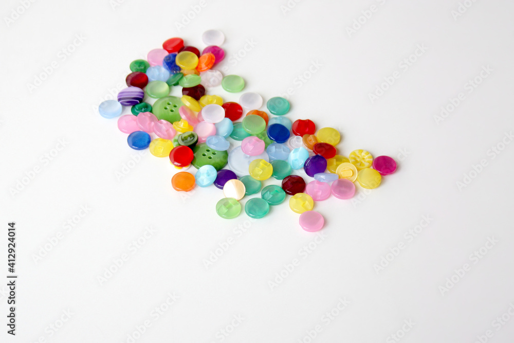Multi-colored sewing buttons lie on a white background. Concept - sewing clothes. Horizontal photo. Selective focus. Multi-colored sewing buttons lie on a white background. Concept - sewing clothes. Horizontal photo. Selective focus.