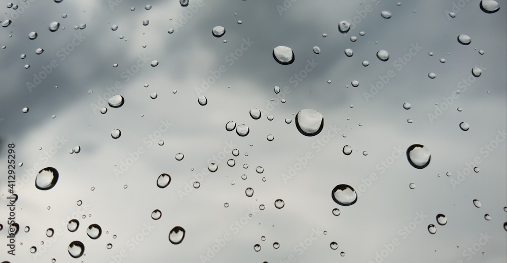 Raindrops on clear window glass in front of gloomy blue sky covered by dark clouds