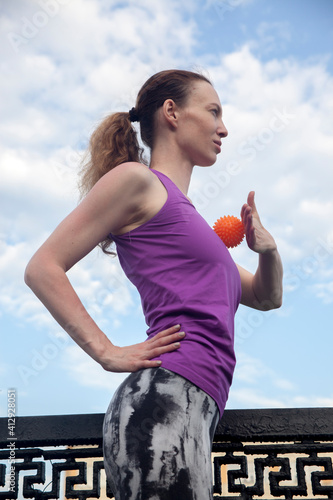 Fototapeta Naklejka Na Ścianę i Meble -  yoga hedgehog .orange bright massage ball girl athlete fitness exercise with a ball in the fresh air in the summer. Fitness Good mood, positive mood, happiness in motion