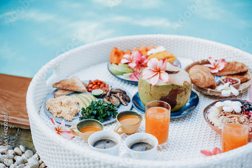 Many of natural and healthy asian food fruits and drinks on white floating table around swimming pool in daytime.