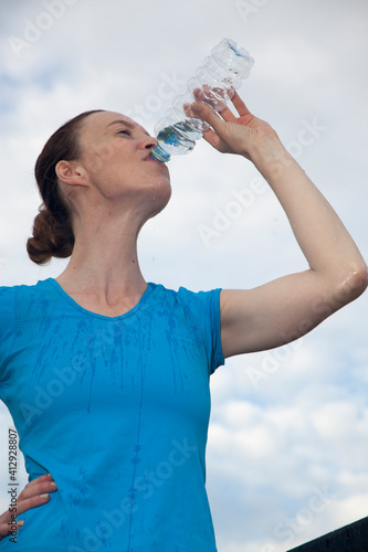 Female athlete drinks water from a bottle. Young woman quenches thirst in hot summer Fitness Good mood, positive mood, happiness in motion. 