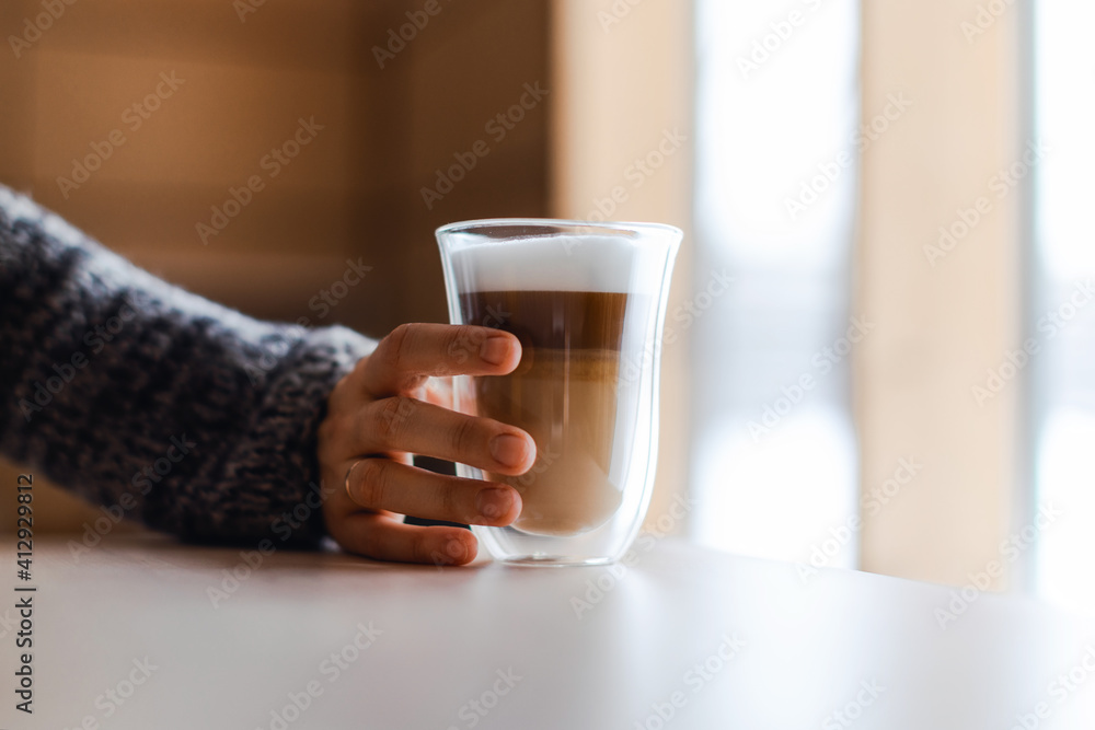 Woman's hand in gray sweater puts milk foam in cappuccino. Woman's hand in gray sweater puts milk foam in cappuccino.