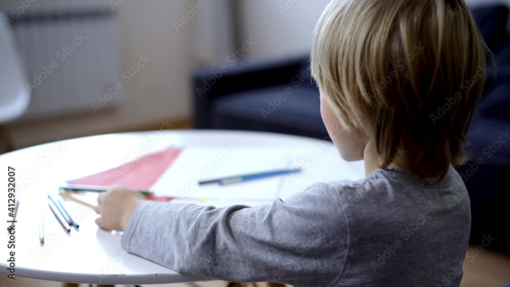 Concentrated little genius boy sitting at table doing homework. Blond Caucasian focused child studying at home in the evening. Education and learning. Concentrated little genius boy sitting at table doing homework. Blond Caucasian focused child studying at home in the evening. Education and learning.