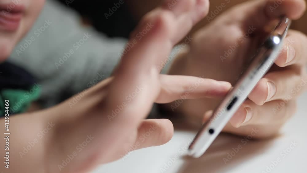 Baby hand taps on phone screen. Close-up of child hand and adult woman hand is holding smartphone, little fingers of toddler move on screen. Slow motion Baby hand taps on phone screen. Close-up of child hand and adult woman hand is holding smartphone, little fingers of toddler move on screen. Slow motion