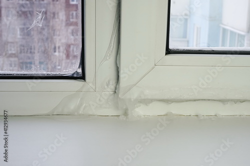 Damage to the window frame snow covered freezing inside the room during severe frost. Close-up of a frozen defective plastic window in a room in winter.	
