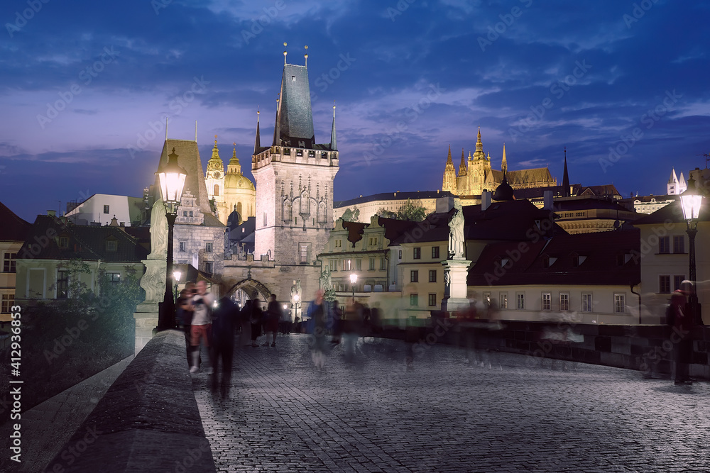 Prague at night. Charles Bridge early in the morning with unrecognizable tourists and town guests waiting on the famous bridge for the sunrise above Bridge Tower