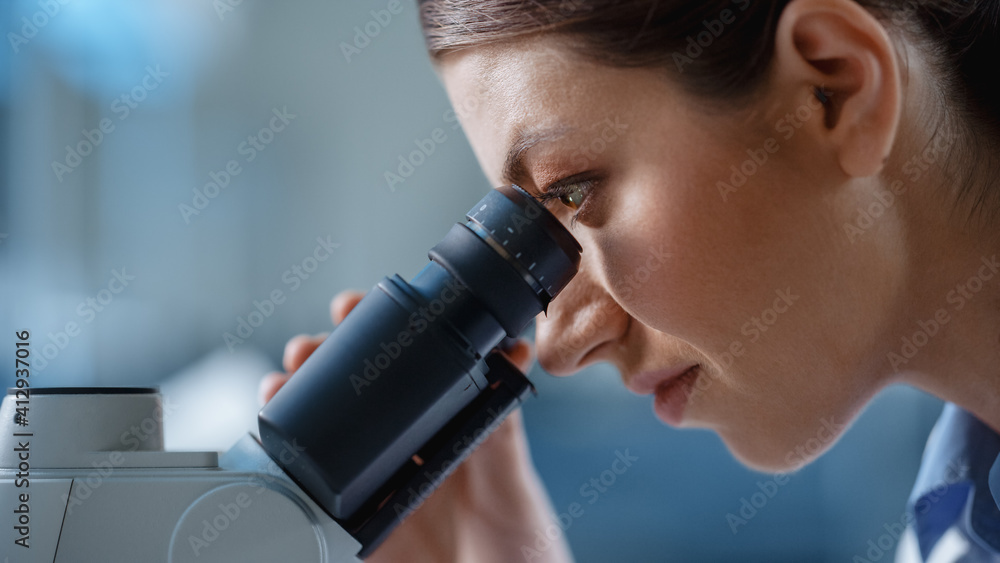 Macro Close-Up Shot of a Beautiful Female Scientist Looking into the Microscope. Woman Microbiologist Working on Molecule Samples in Modern Laboratory with Technological Equipment. Macro Close-Up Shot of a Beautiful Female Scientist Looking into the Microscope. Woman Microbiologist Working on Molecule Samples in Modern Laboratory with Technological Equipment.