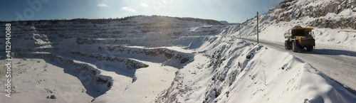 Panorama of a snow-covered limestone quarry with a mining dump truck in the foreground. Mining machinery.