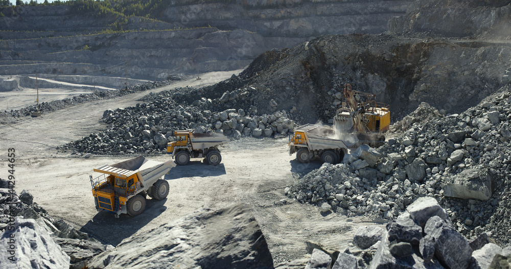 Heavy mining trucks near the excavator awaiting their turn to stone ore loading in limestone quarry, industrial panorama. Heavy mining trucks near the excavator awaiting their turn to stone ore loading in limestone quarry, industrial panorama.