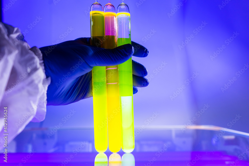 Fluorescein glowing in flask under ultraviolet light. A closeup of man hand holding up a vial