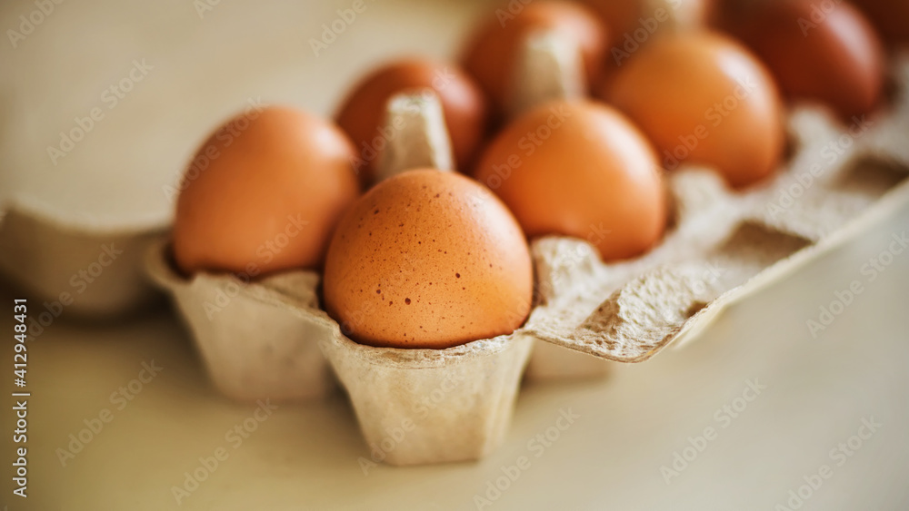 Brown chicken eggs lie in a cardboard store box, are on a white table and illuminated by sunlight. Healthy food for breakfast. Brown chicken eggs lie in a cardboard store box, are on a white table and illuminated by sunlight. Healthy food for breakfast.