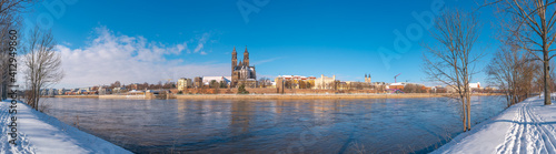 Panoramic view over Magdeburg historical downtown in Winter with icy trees and snow during sunrise in the morning with warm illumination and blue sky, Germany.