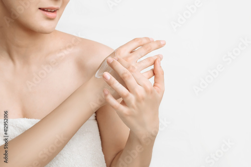 young attractive woman smears hand cream on a white background copy space  a woman takes care of the body  moisturizes her hands