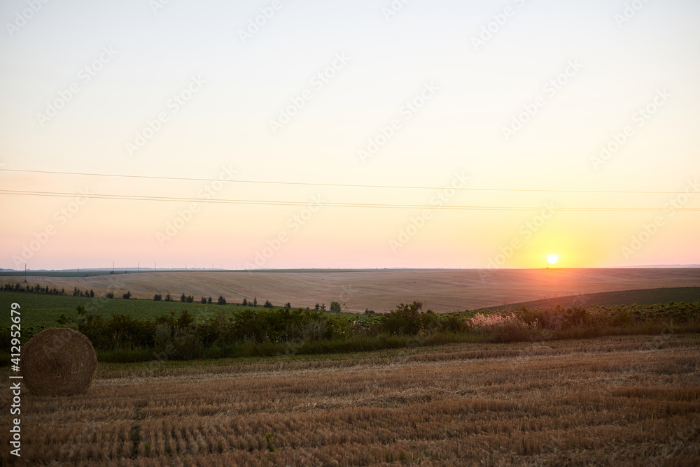 Sunset over natural field landscape in summer with light blue sky. Stubble field with straw bale. Agricultural rural background. Ecological food production.