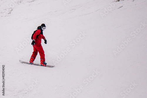 A guy in a red jumpsuit eating freeride on a snowboard on a snowy slope