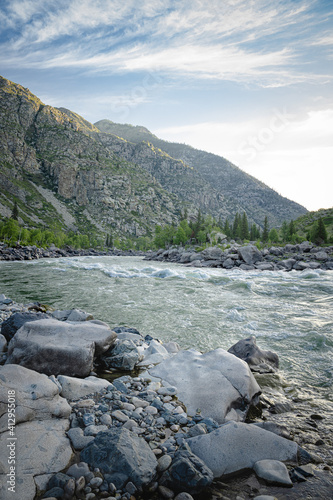 A stormy rapids river flows among rocky banks in the highlands. Beautiful landscape with sunlit mountains. Morning in the wild. The Katun River, Altai Republic.