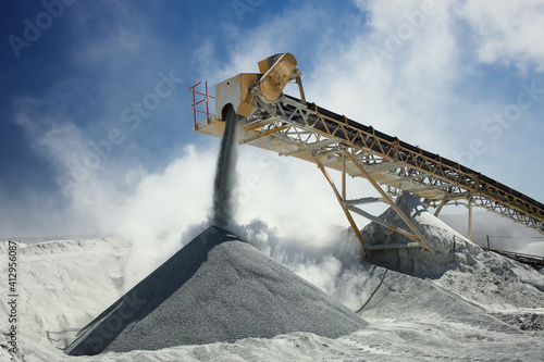 Details of stone crushing equipment at the mining factory in a cloud of dust against the blue sky, close-up. Quarry mining machinery.
