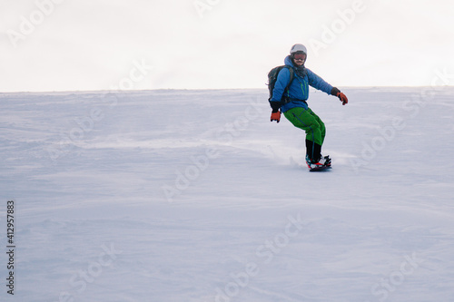 A guy in a bright suit rides a freeride on a snowboard on a snowy slope