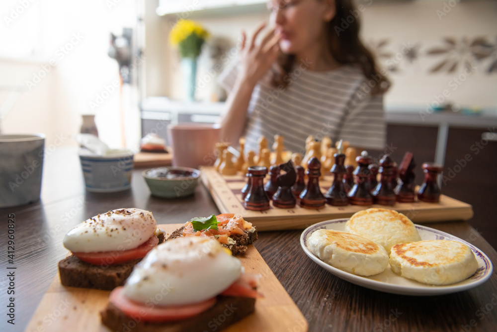 Young woman having breakfast while playing chess (Selective focus)