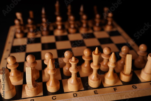 Close up of black chess pieces on board. Two rows of wooden figures on chessboard on black background. Concept of intelligent  logical and strategic game
