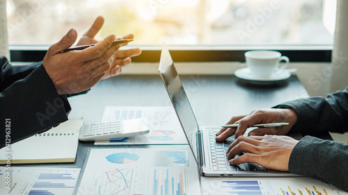 Fotografia Meeting two business people with a laptop and analyzing the cost graph on the desk in the orange-lit conference room