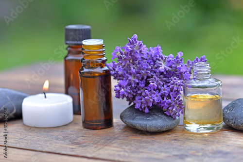 bottle of essential oil and bouquet of lavender flower arranged on a wooden table with a canddle