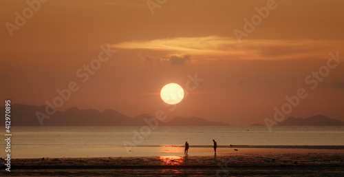 Sunset sea with people silhoette on the beach and big sun above islands on horizon