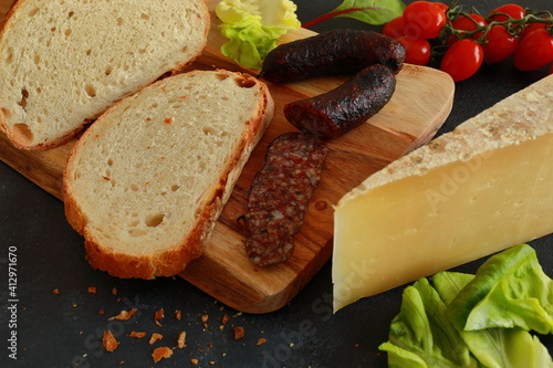 Homemade crispy bread with traditional salami, cheese and vegetables on wooden board with dark background