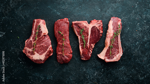 Set of raw steaks - t-bone, tomahawk, striploin, tenderloin, new york steak. On a black stone background. Top view.