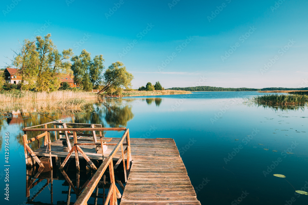 Naklejka premium Old Wooden Fishing Pier Near Summer Lake Or River. Calm Water In Beautiful Summer Sunny Day.