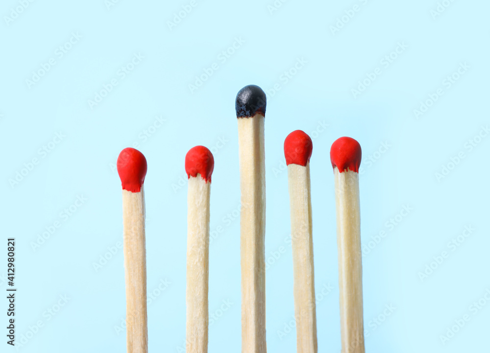Row of whole matches and burnt one on light blue background. Uniqueness concept Row of whole matches and burnt one on light blue background. Uniqueness concept