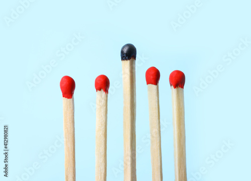 Row of whole matches and burnt one on light blue background. Uniqueness concept