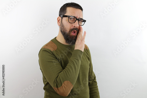Man with beard and glasses wearing casual clothes hand on mouth telling secret rumor, whispering malicious talk conversation