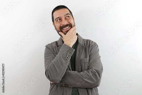 Bearded man wearing casual clothes with hand on chin thinking about question, pensive expression. smiling with thoughtful face. doubt concept.