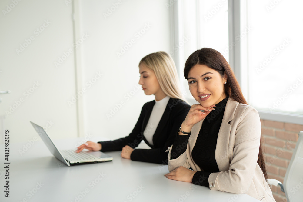 two beautiful young women at the table in the office with a laptop two beautiful young women at the table in the office with a laptop