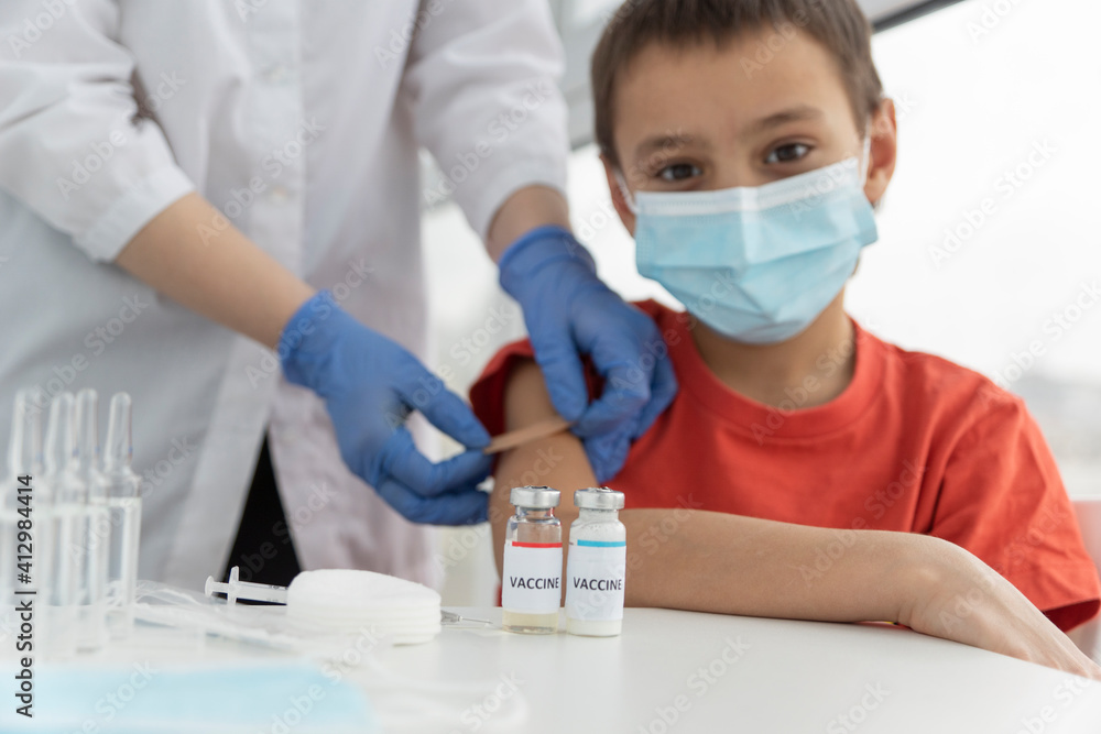 Fototapeta premium happy boy in medical mask after vaccination from covid. Doctor's hands glue plaster on injection site. Vaccination concept